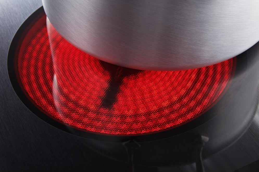 Close-up of a stainless steel pot heating on a red glowing ceramic glass cooktop burner from kitchen appliances collection