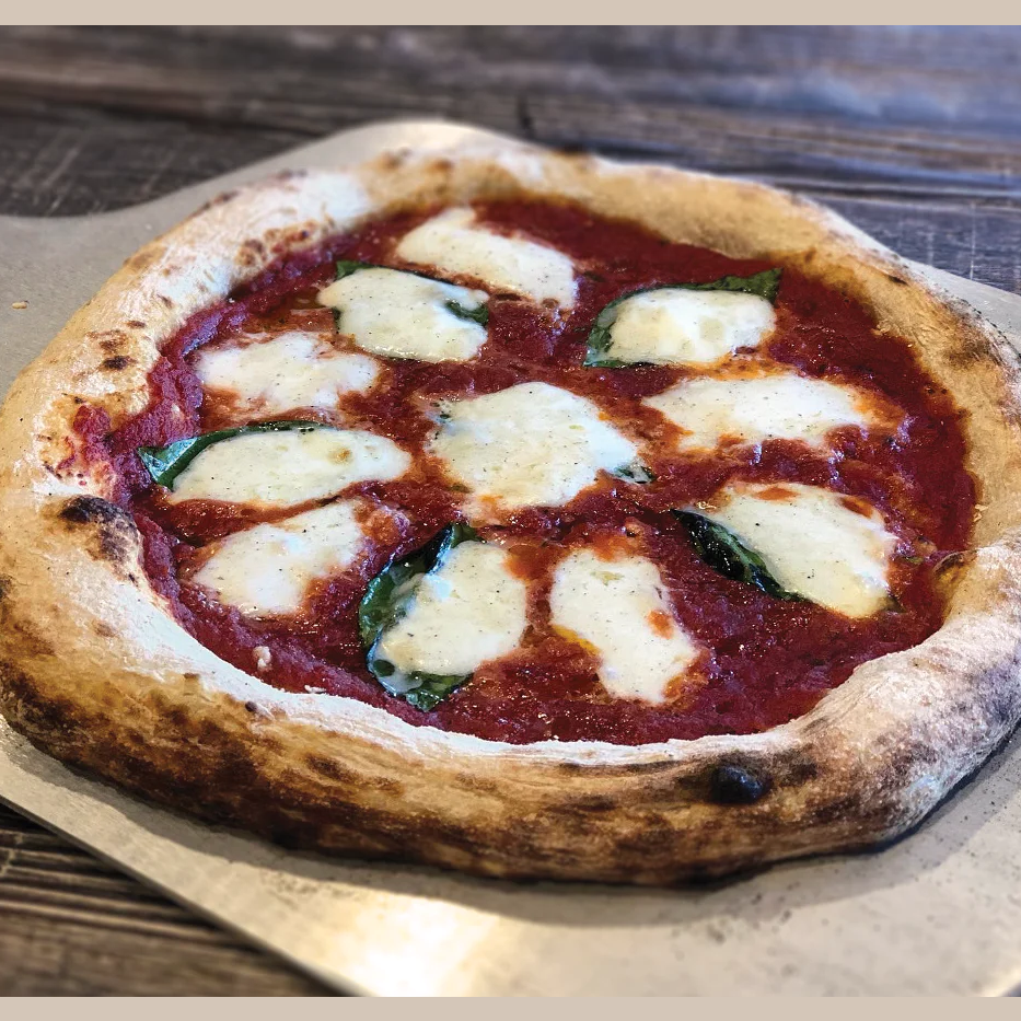Neapolitan style pizza with fresh mozzarella and basil leaves on a wooden surface for outdoor living grilling collections
