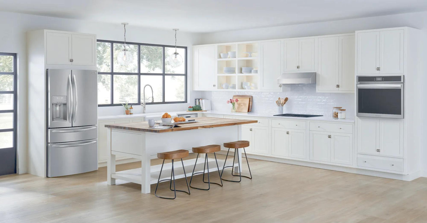 Bright modern kitchen with white cabinets, large island with wooden stools, stainless steel fridge, and built-in single electric wall oven
