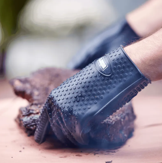 Black silicone grilling glove with textured grip securely handling large smoked meat in outdoor cooking setting