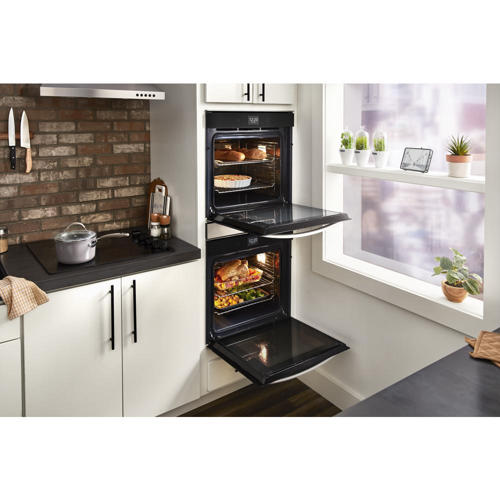 Open double wall oven with convection cooking baking dishes simultaneously in modern kitchen with brick backsplash and white cabinetry