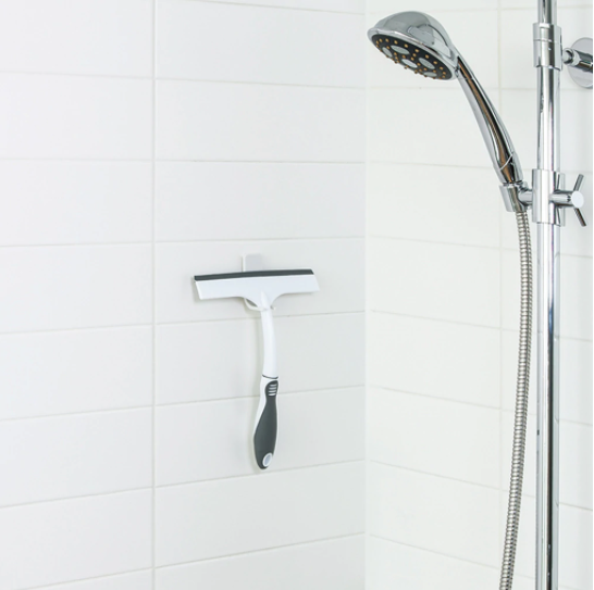 White and grey shower squeegee with ergonomic grip hanging in bathroom near chrome shower head in bath collection