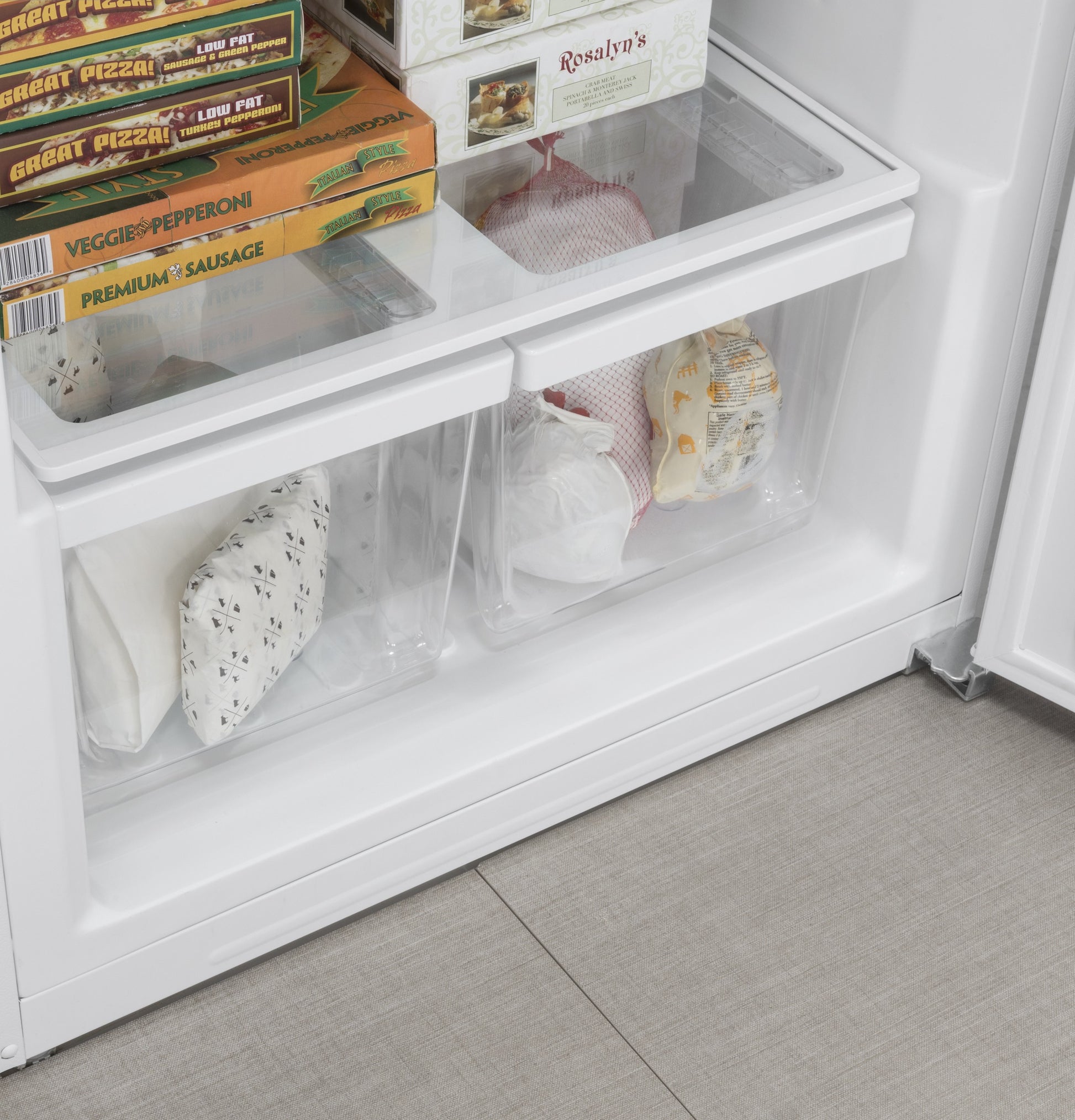 Lower freezer compartment with clear bins storing packaged frozen food inside an upright freezer from appliances collection