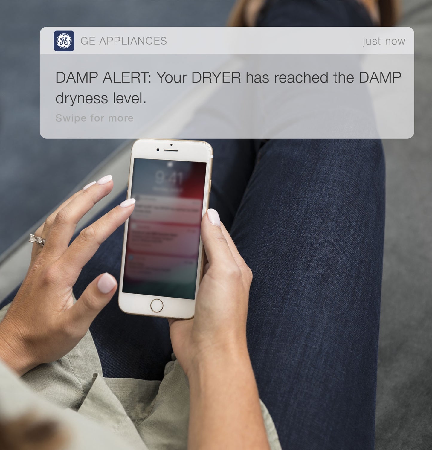 Person holding smartphone showing GE Appliances app notification about dryer dampness alert for smart home use