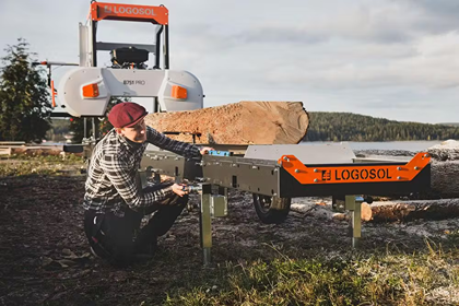 Man adjusting a portable Logosol band sawmill cutting large logs outdoors for home improvement projects