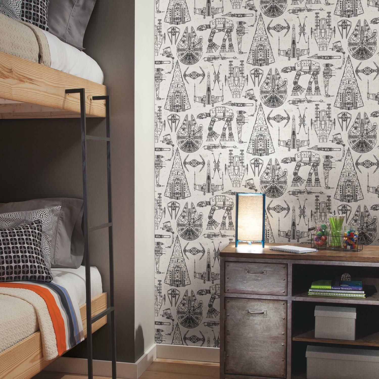 Monochrome peel and stick wallpaper with detailed Star Wars ship blueprints decorating a bedroom wall behind a wood bunk bed and metal desk