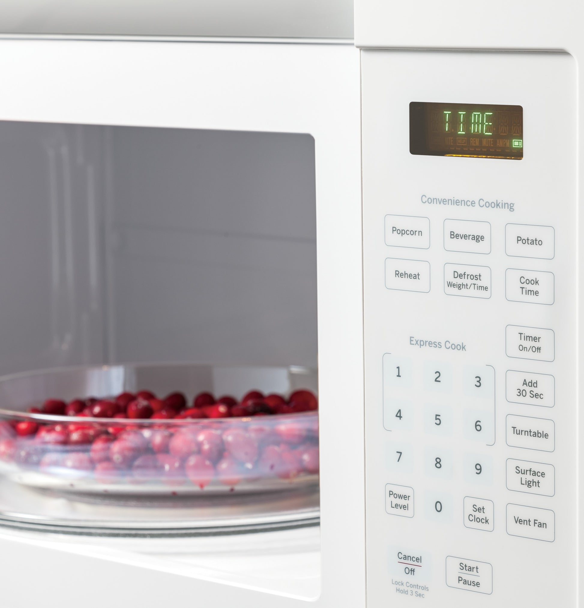 White over-the-range microwave oven with digital control panel and turntable containing a bowl of red berries