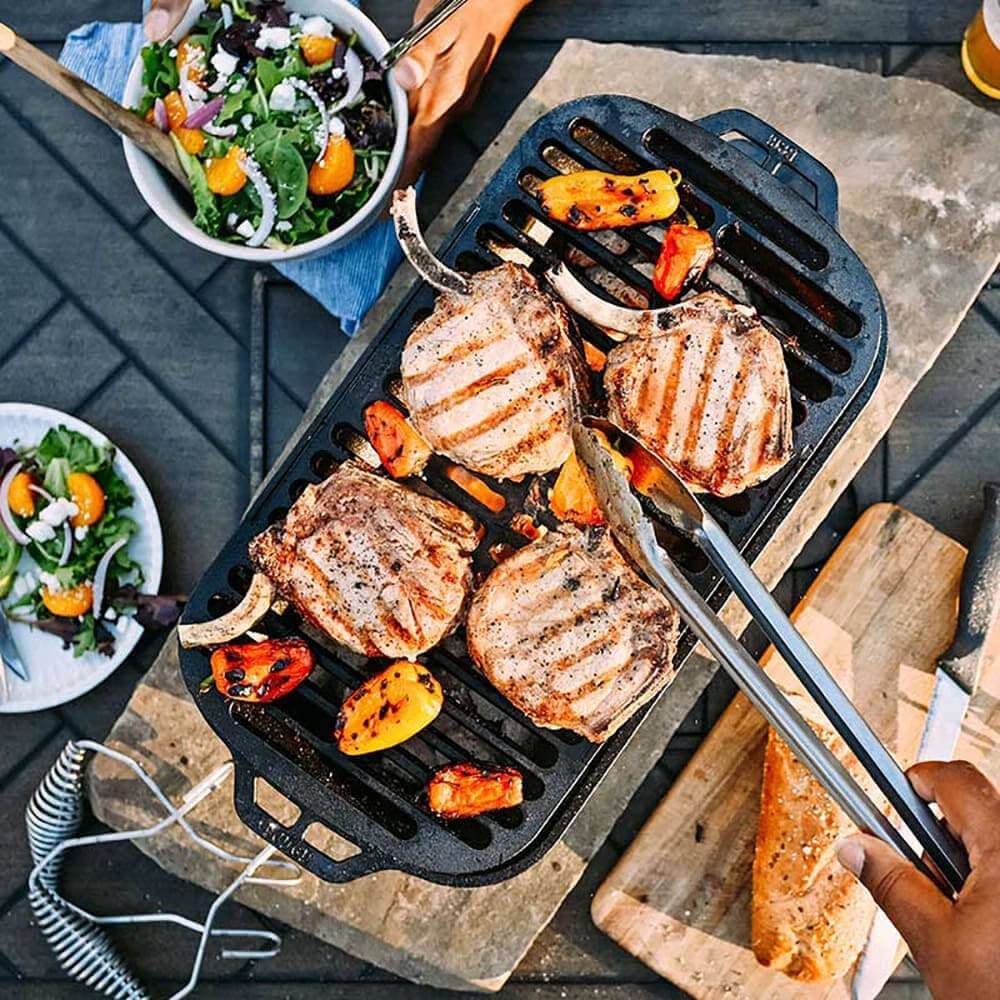 Cast iron grill with four grilled pork chops and vegetables, surrounded by fresh salad and bread, kitchenware collection