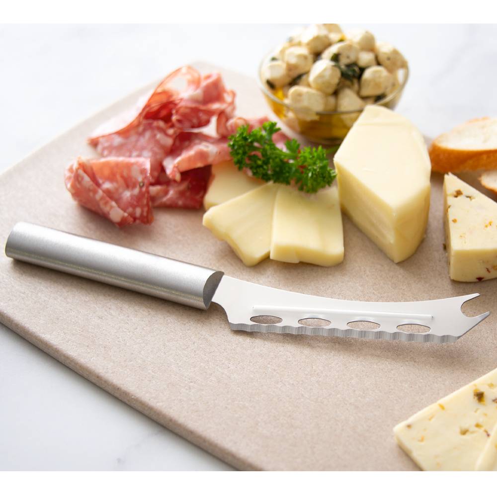 Serrated stainless steel cheese knife with holes and forked tip on cutting board with cheese and charcuterie in kitchenware collection