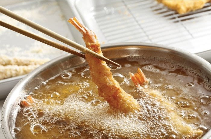Chopsticks holding breaded shrimp over bubbling oil in fryer, illustrating use of kitchen gadget for frying foods