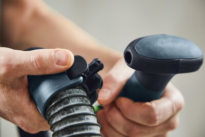 Hands attaching a Festool PLANEX hose clip to a flexible hose on a power tool in a home improvement setting