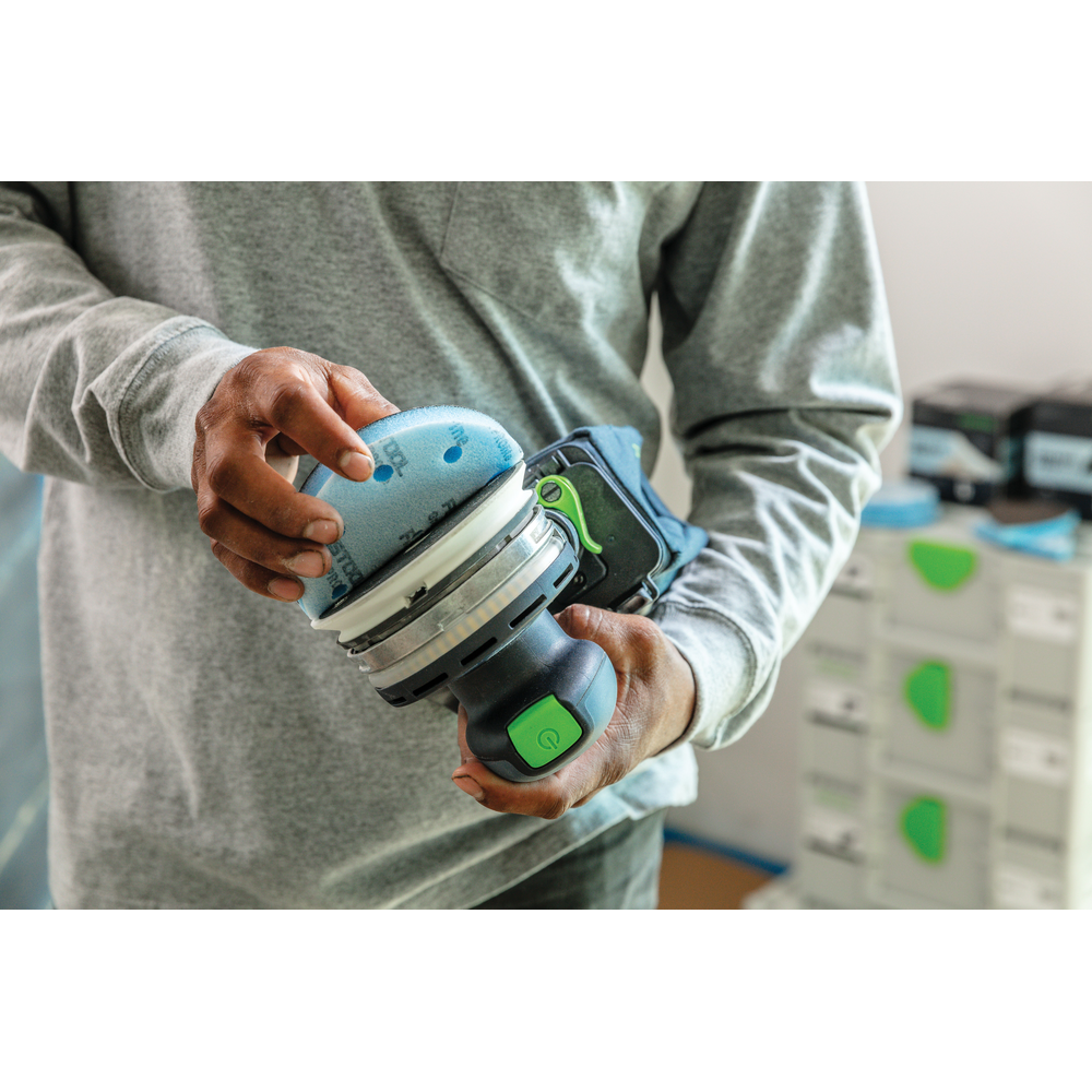 Person attaching blue foam-backed abrasive disc to cordless power sander in Festool tool accessories for home improvement