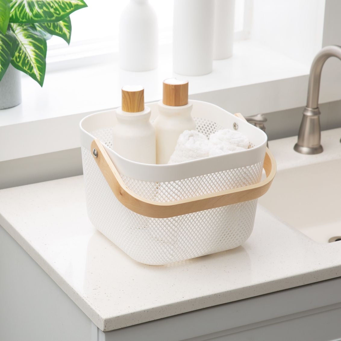 White plastic mesh basket with wooden handle holding lotion bottles and towels for bathroom storage under $50 collections