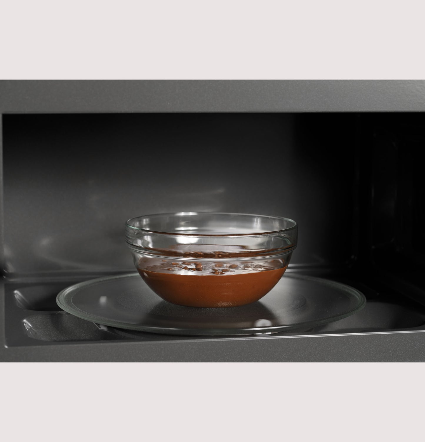 Glass bowl with chocolate mixture heating on the turntable inside an over-the-range microwave oven from kitchen appliances