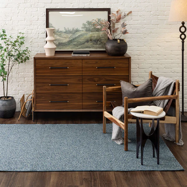 Blue textured woven rug in modern living space with wooden dresser, armchair, decorative vase, and floor lamp