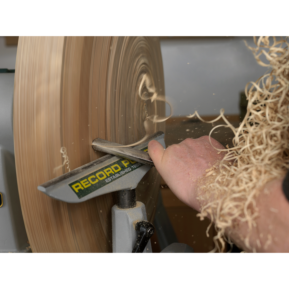 Close-up of a woodworking lathe shaping a spinning wooden bowl using a sharp steel gouge in woodworking tools under $100 collection