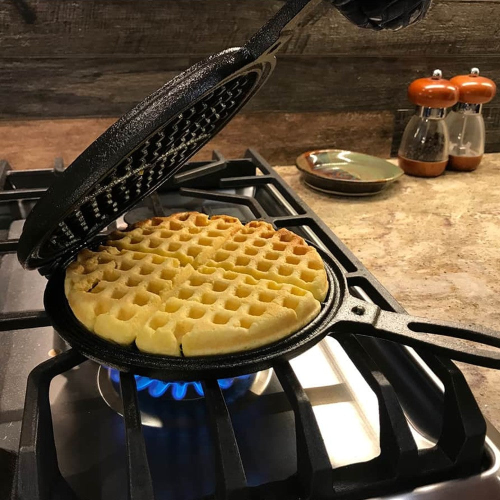 Stovetop cast iron waffle maker with long handle cooking waffle over blue gas flame on kitchen stove burner