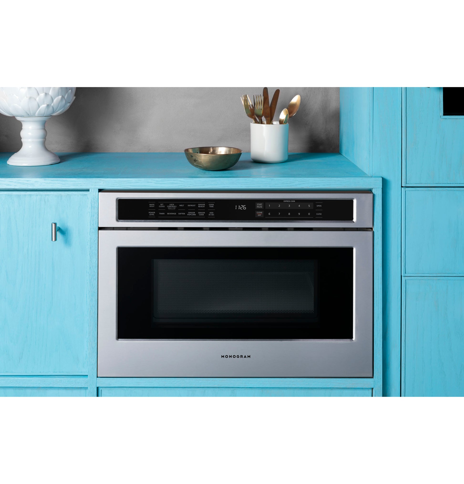 Built-in stainless steel microwave drawer integrated into blue kitchen cabinetry with utensils on countertop above