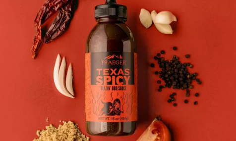 Bottle of Traeger Texas Spicy BBQ sauce surrounded by garlic, black pepper, dried chili, tomato, and brown sugar under $50