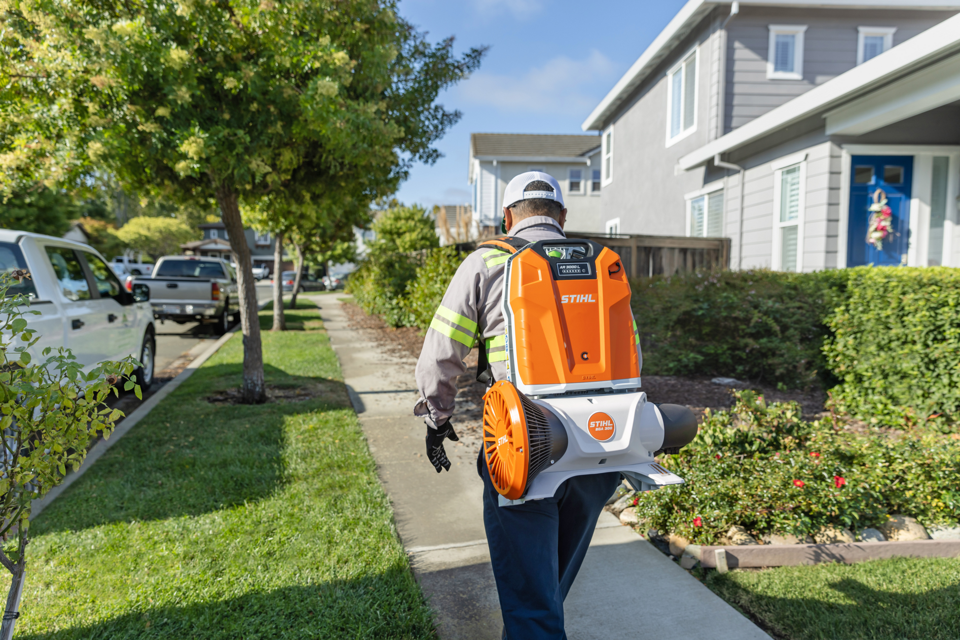 Worker wearing backpack-style STIHL battery blower clearing sidewalk in residential neighborhood during home maintenance