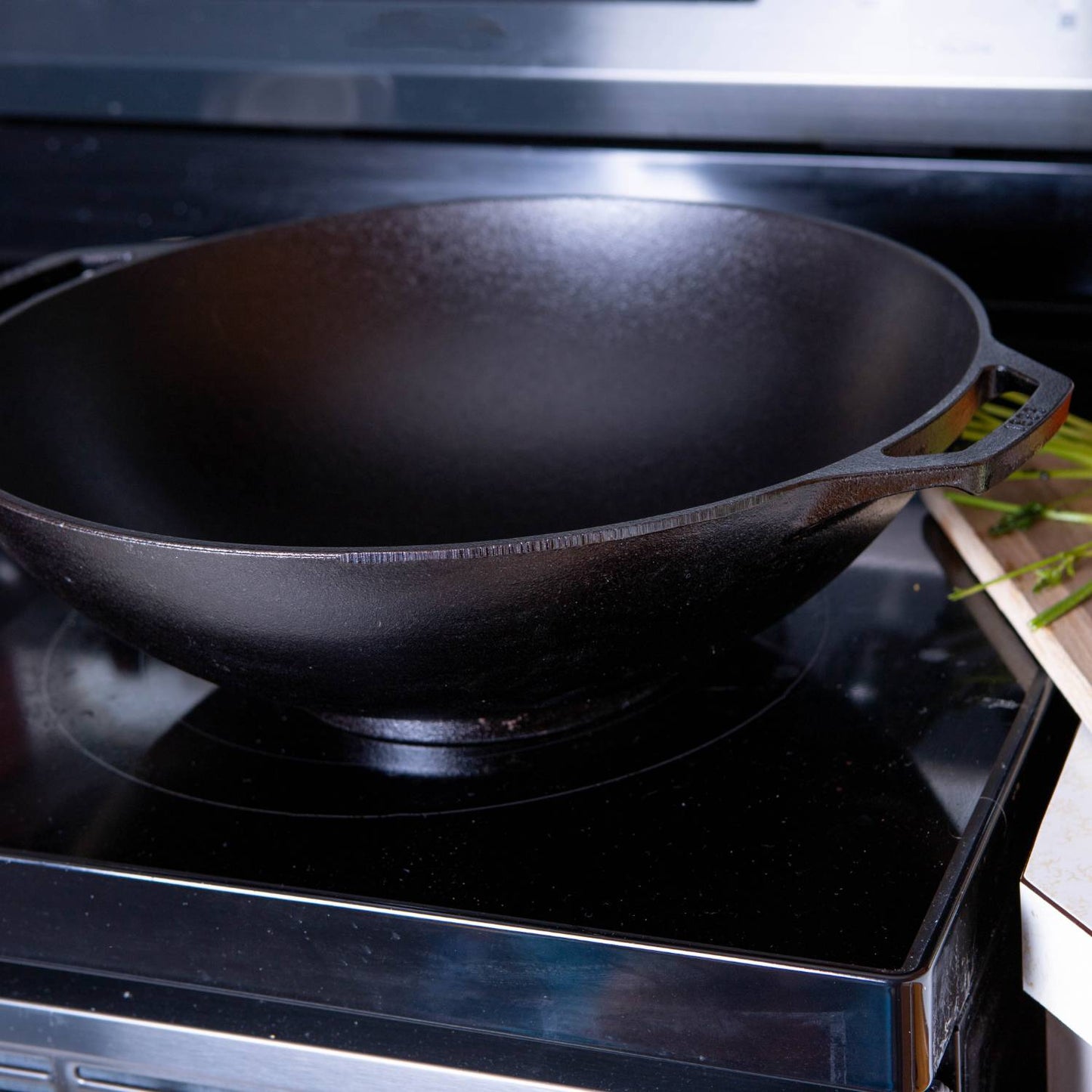 Seasoned wide-base cast iron wok on stovetop with handle, part of kitchenware and Lodge Cast Iron collections under $100