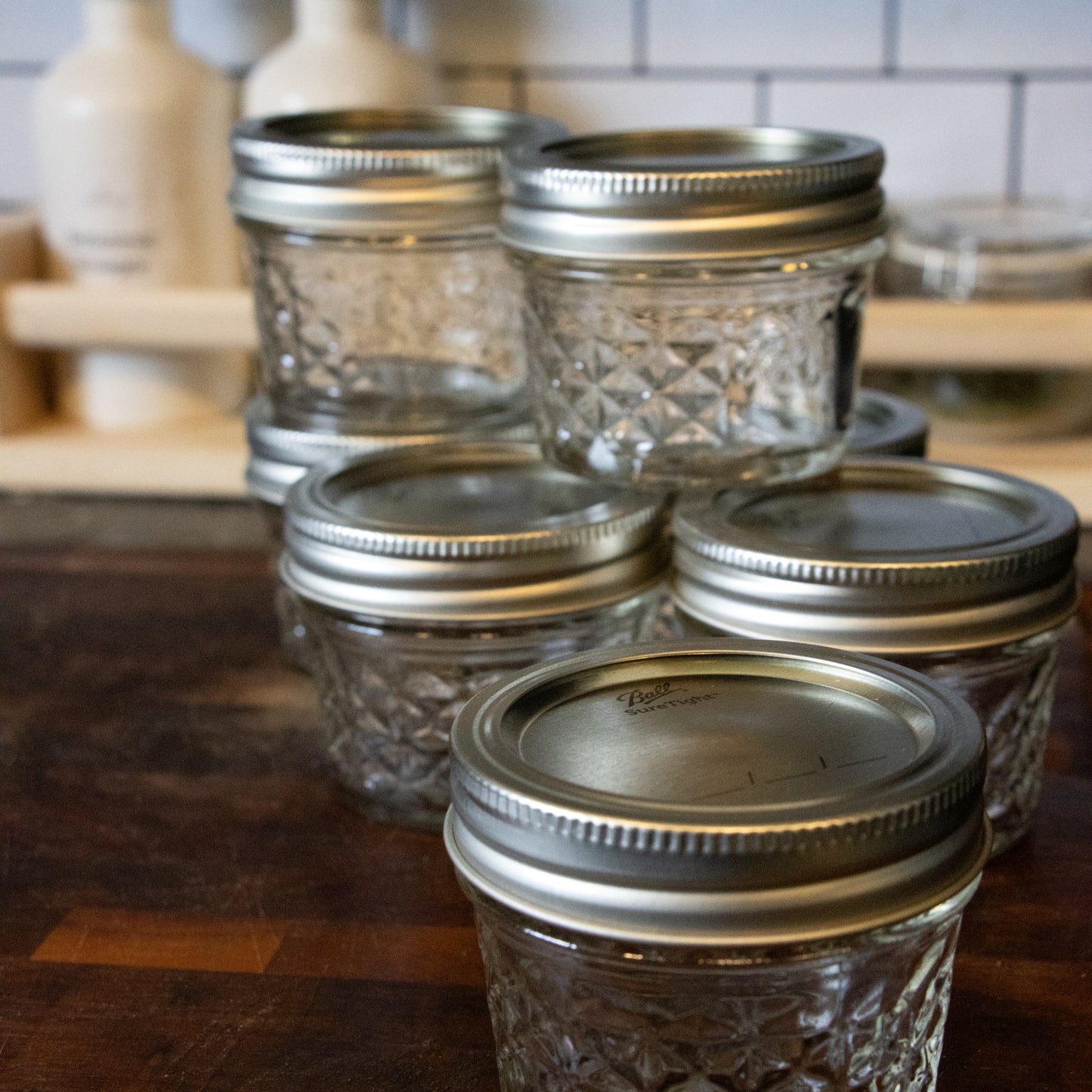 Set of clear glass jars with silver screw-on lids arranged on wooden surface in kitchen setting