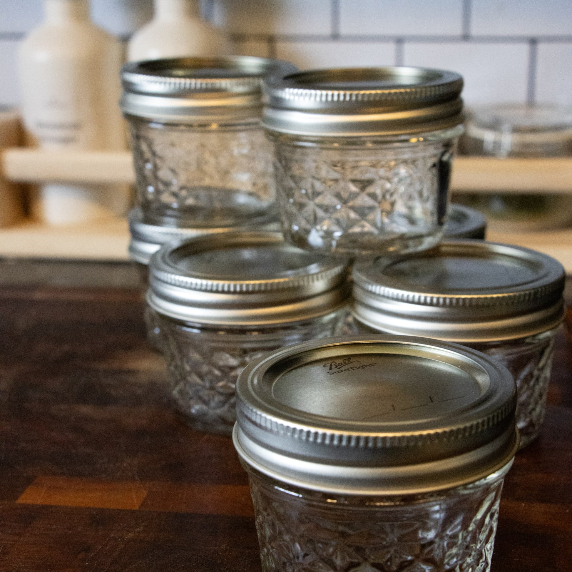 Set of clear glass jars with silver screw-on lids arranged on wooden surface in kitchen setting