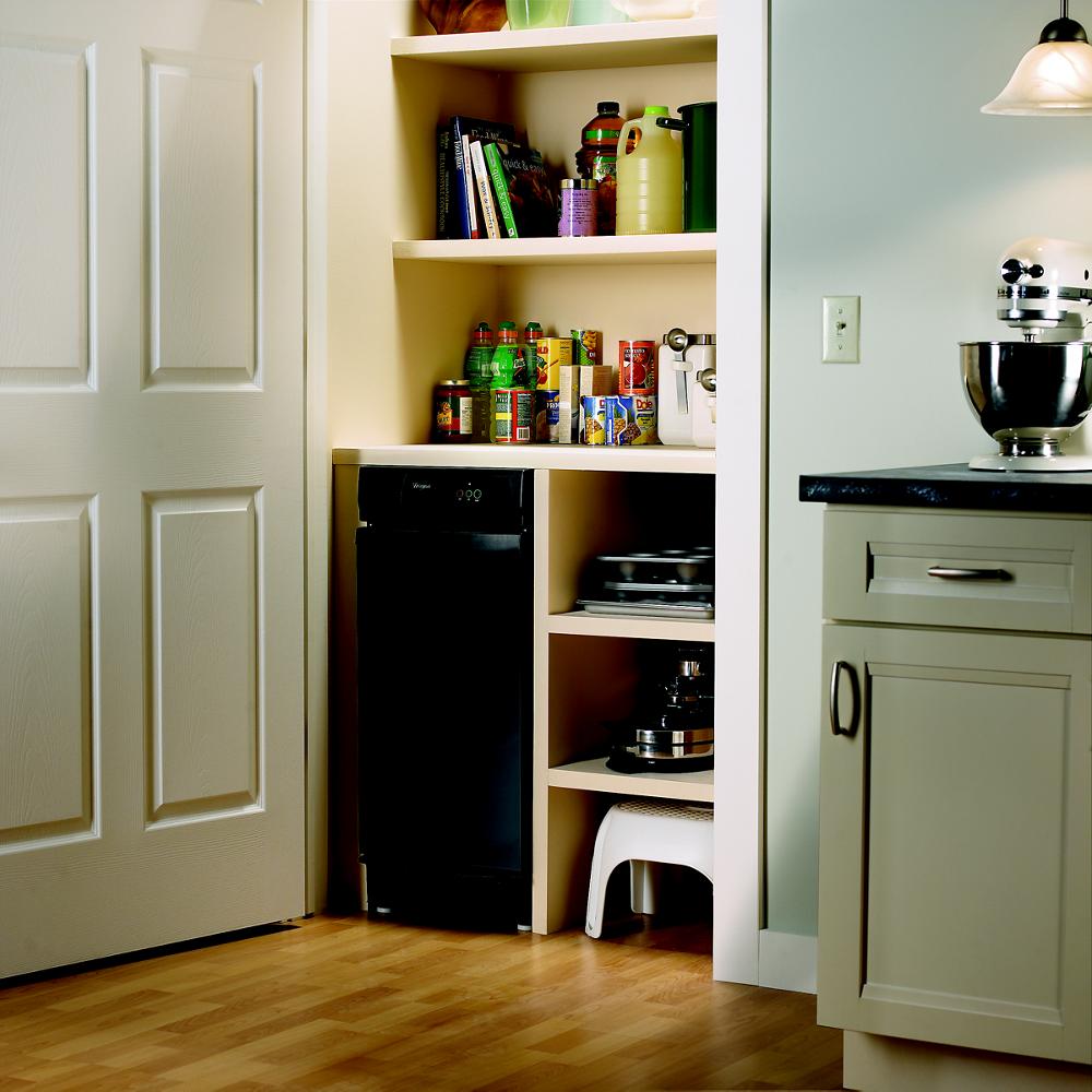 Black 15-inch convertible trash compactor installed in pantry with wooden shelves and kitchen cabinetry nearby