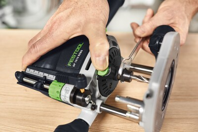 Hands adjusting a compact Festool router on a wooden surface for precise home improvement tool use