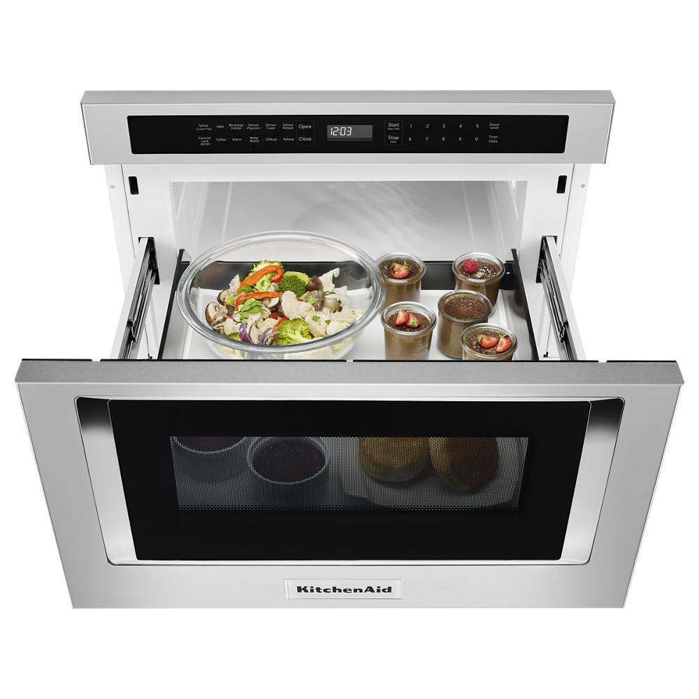 Top view of open stainless steel microwave drawer with digital display, containing glass bowl of vegetables and dessert cups from KitchenAid collection