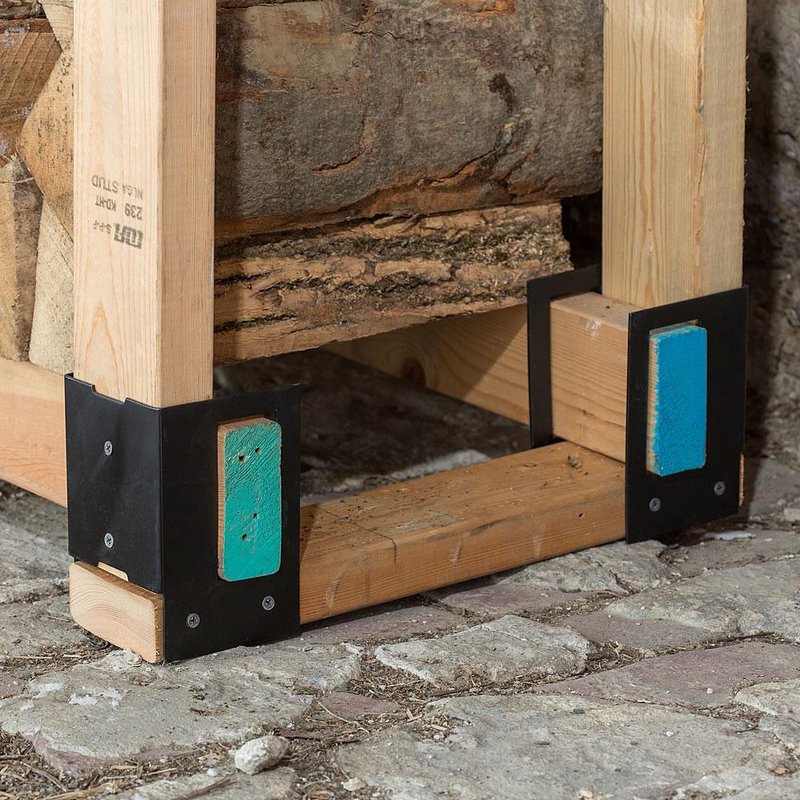 Black metal brackets reinforcing wooden logs stacked on cobblestone floor for home improvement tools