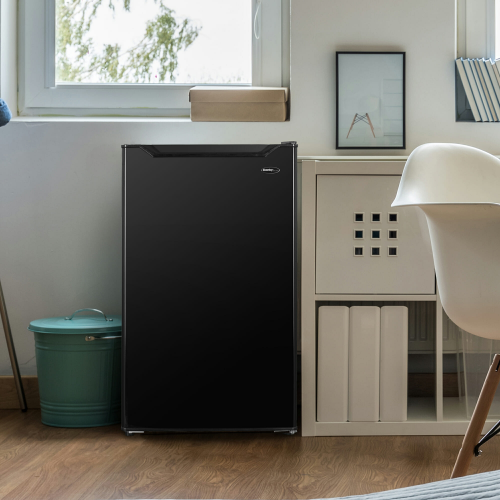 Compact black refrigerator with smooth finish placed next to white storage cabinet in modern kitchen setting