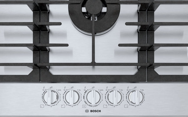Close-up of stainless steel gas cooktop with five control knobs and black burner grates from Bosch appliances.