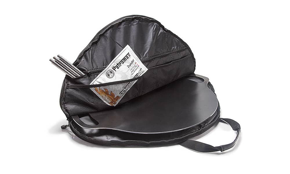 Black nylon storage bag open with round griddle inside and mesh pocket holding instructions and tools for camping gear