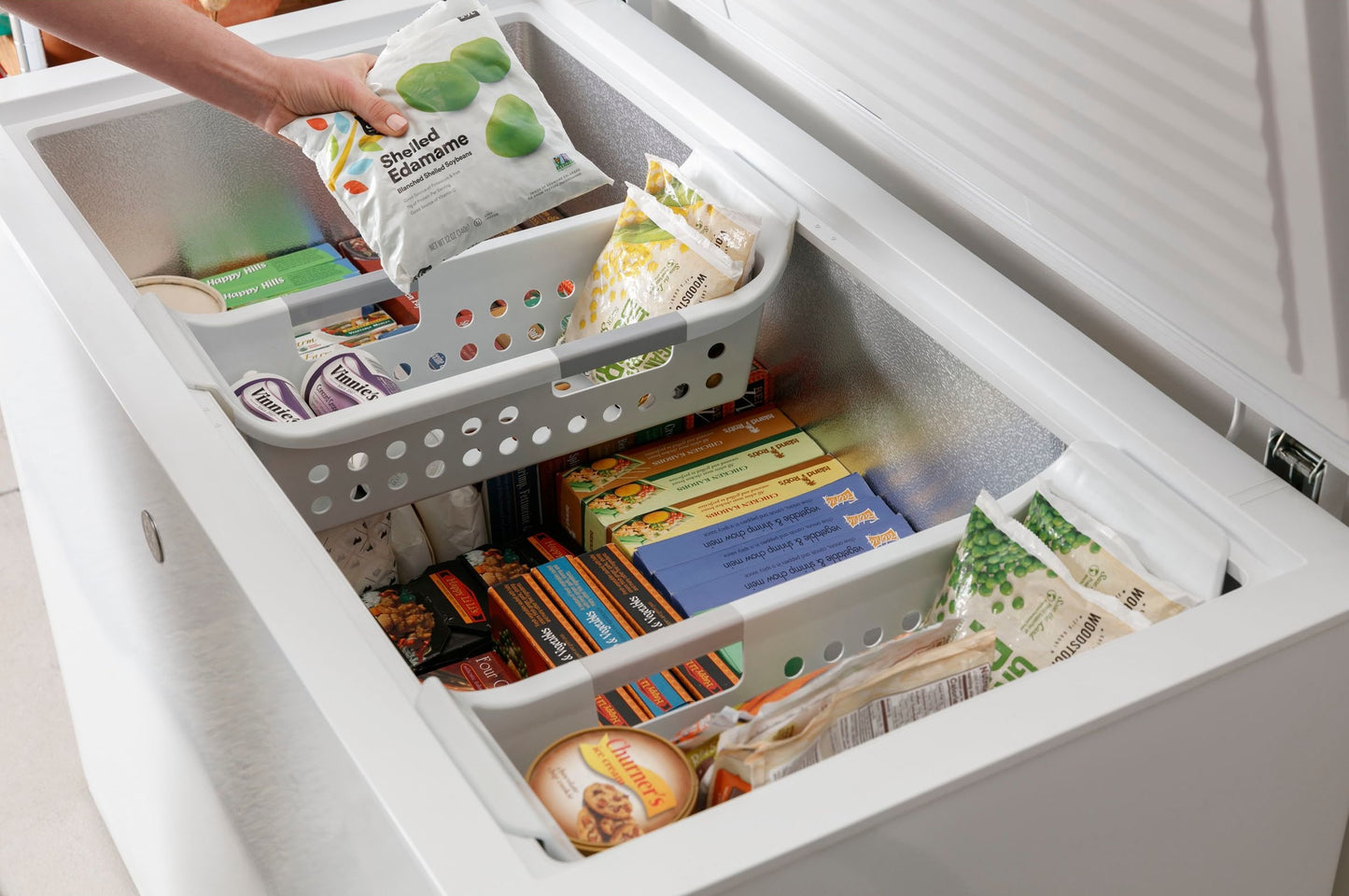 Open manual defrost chest freezer filled with frozen foods and organized with removable storage baskets