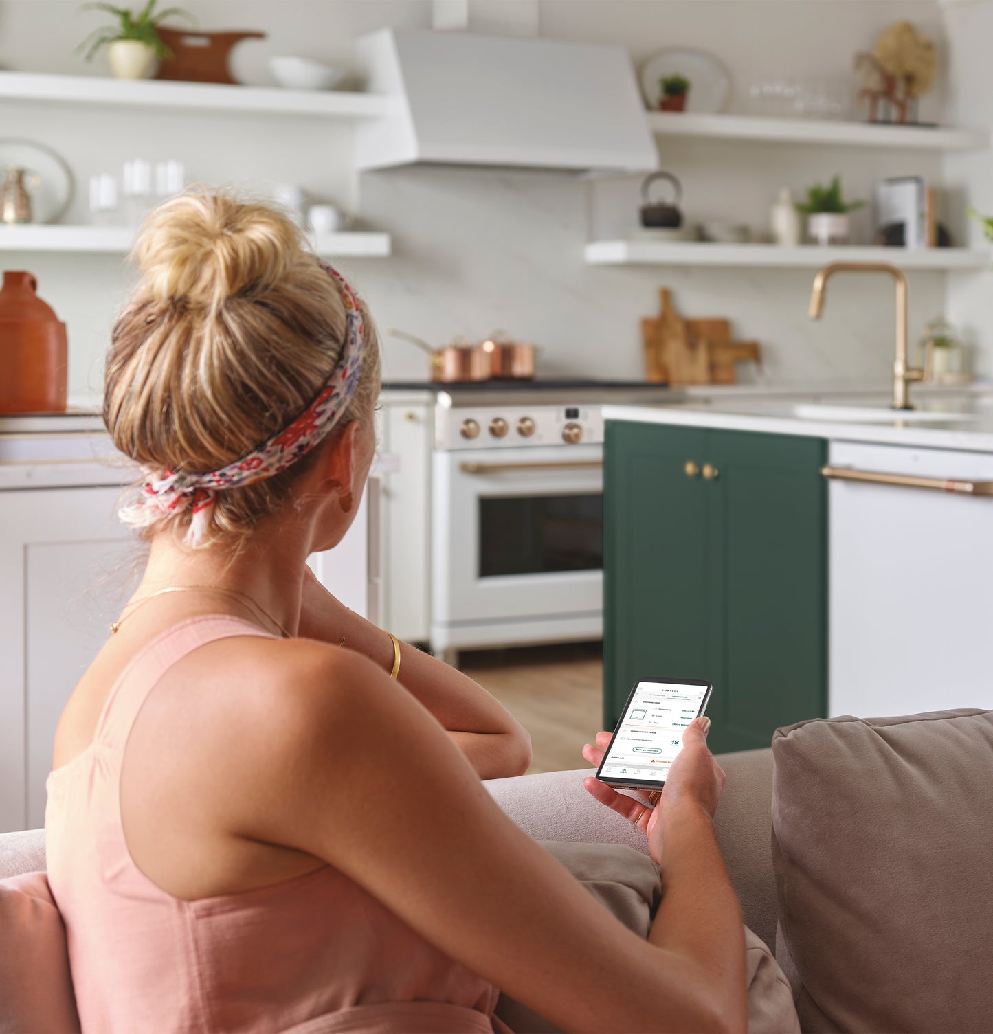 Woman using smartphone to control smart kitchen appliances in modern kitchen with green cabinetry and white range hood