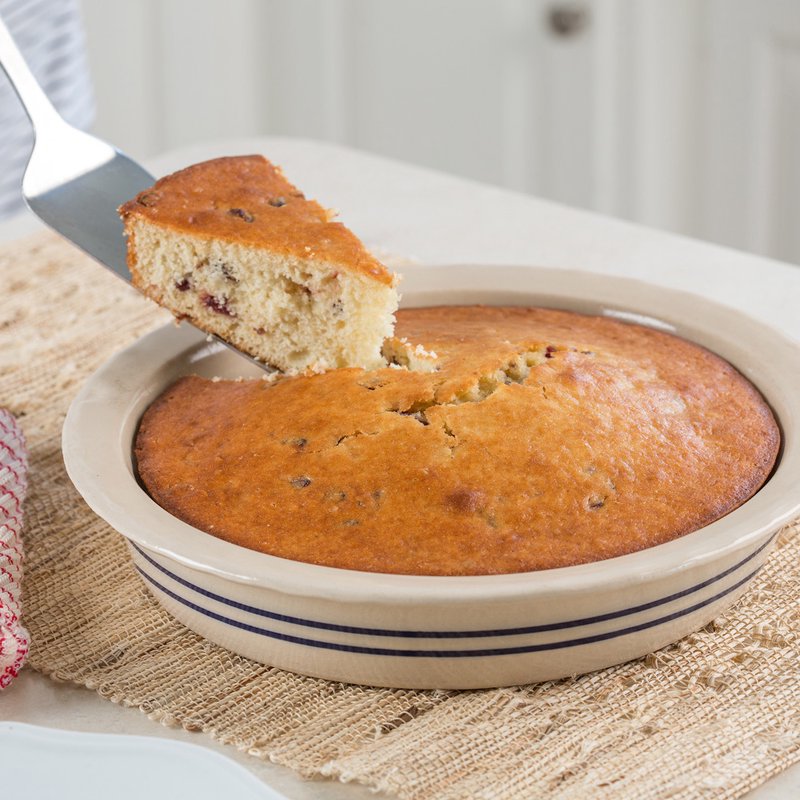 Hand-thrown stoneware pie pan with blue stripes holding freshly baked cake on woven placemat in kitchenware setting