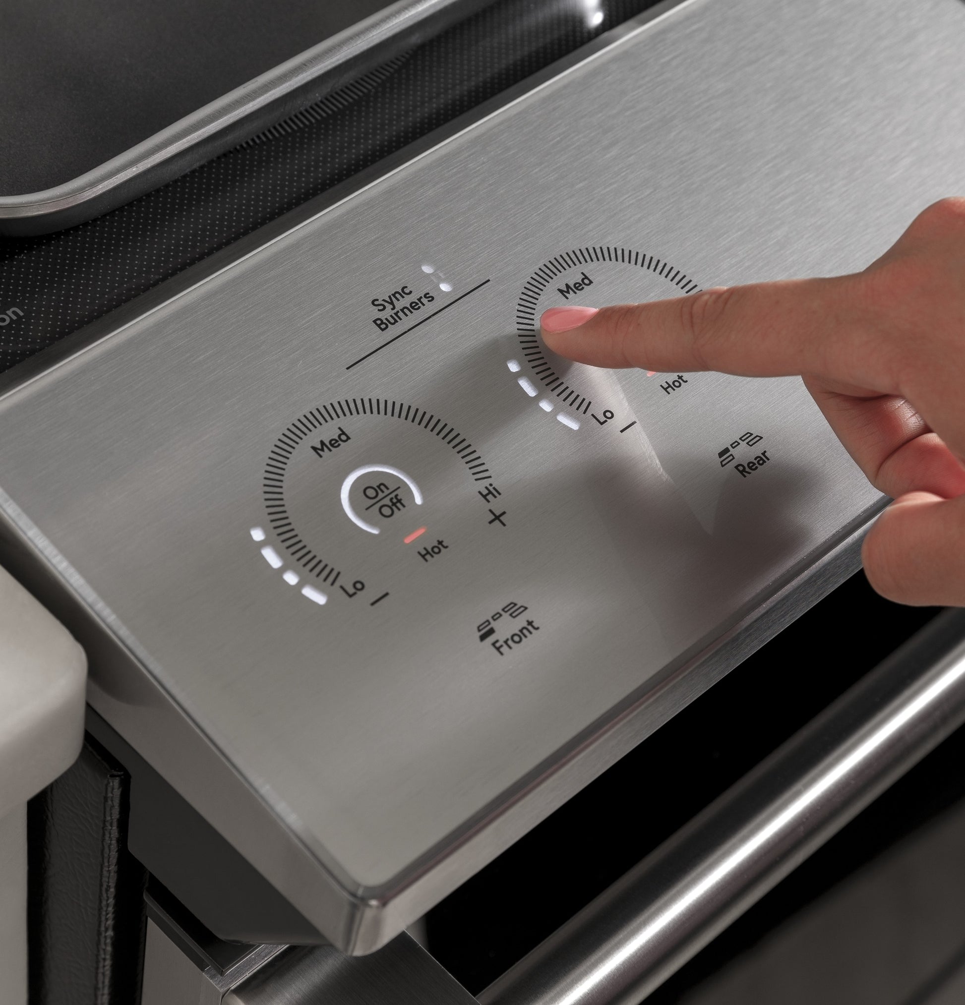 Hand adjusting medium heat setting on stainless steel front control panel of induction cooktop range in kitchen
