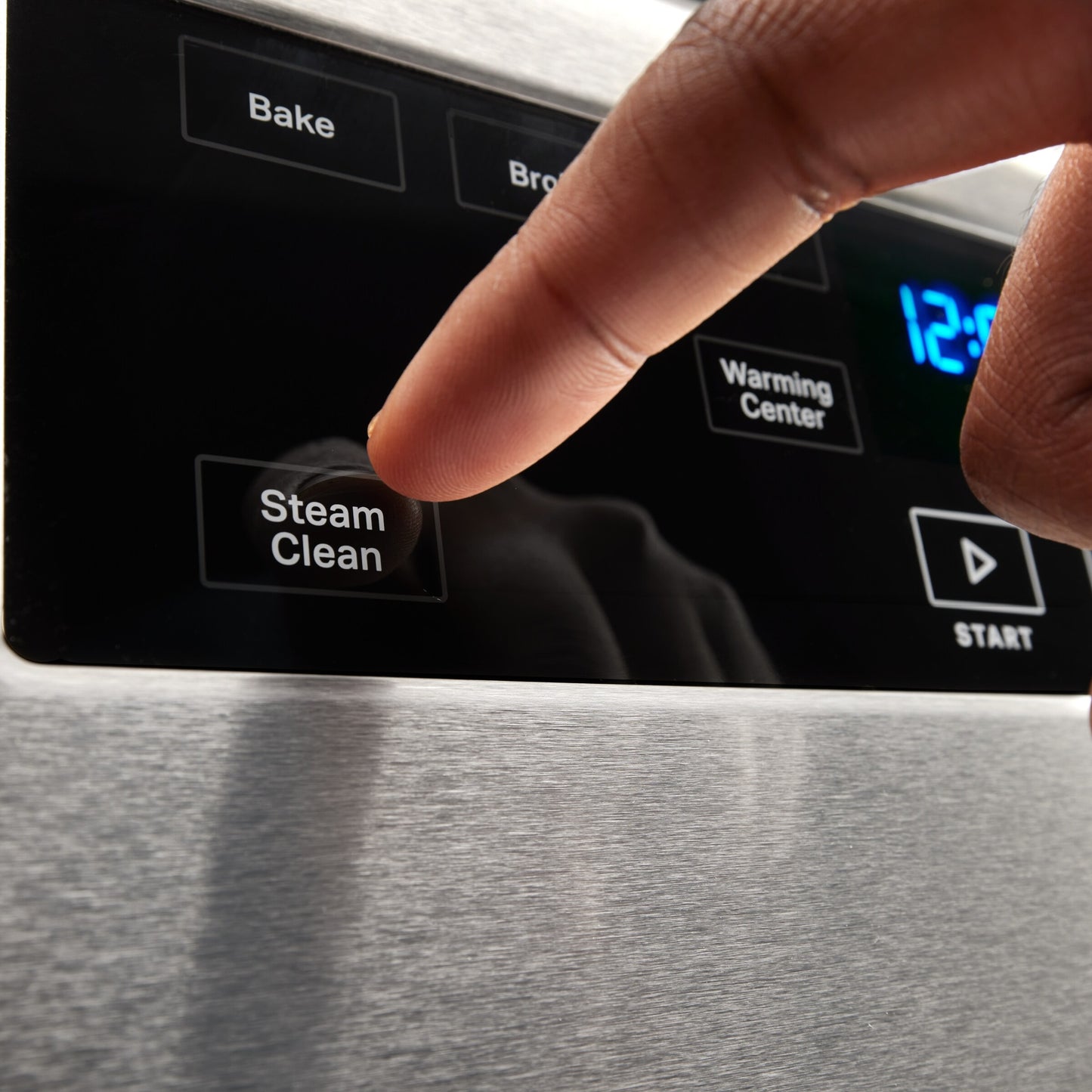 Close-up of finger pressing steam clean button on stainless steel 30-inch electric range control panel