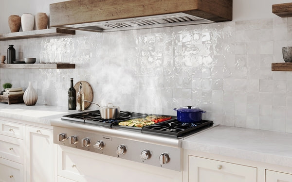 Modern kitchen with stainless steel custom insert range hood and gas cooktop cooking multiple dishes