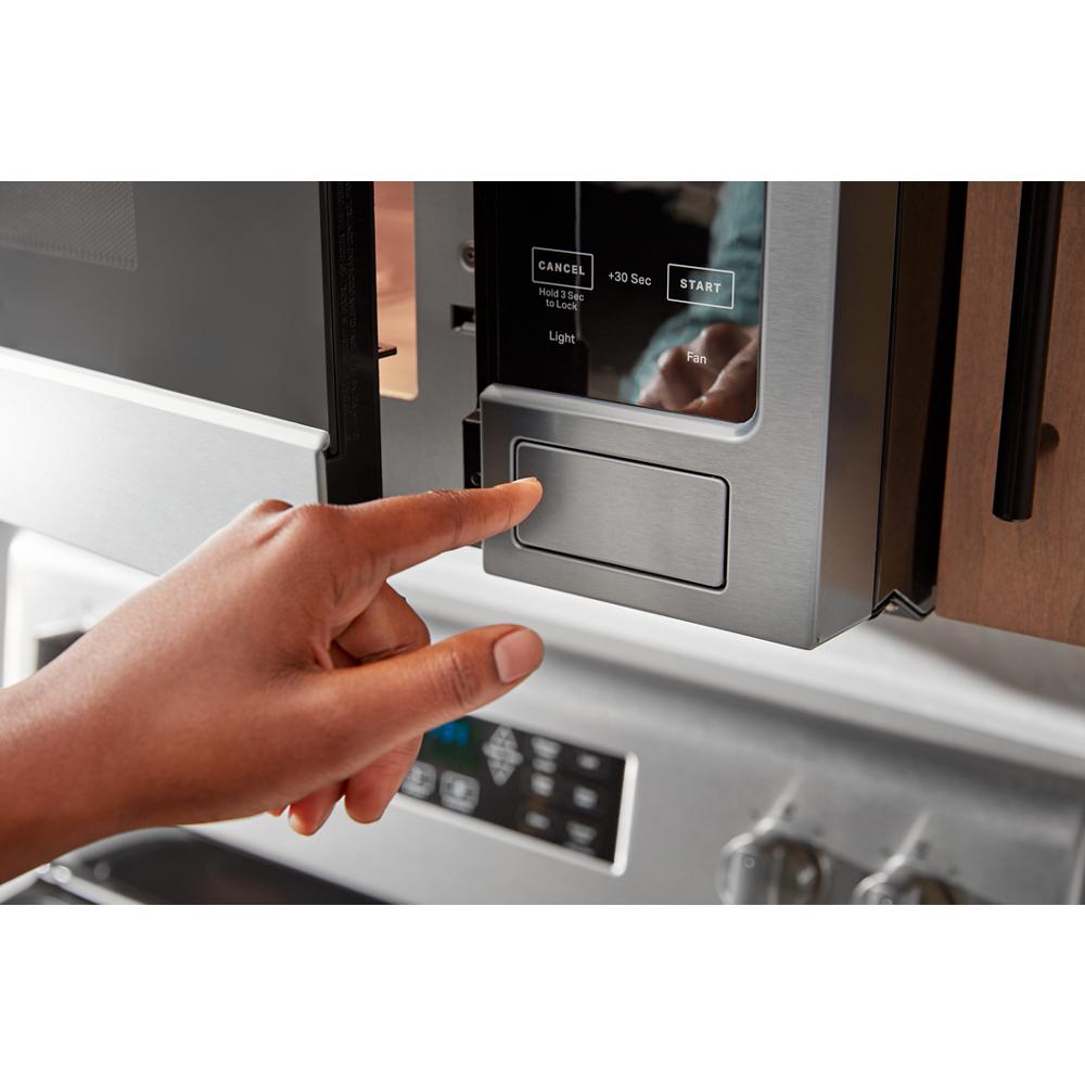 Close-up of hand pressing digital control panel on stainless steel over-the-range microwave in kitchen appliance setting