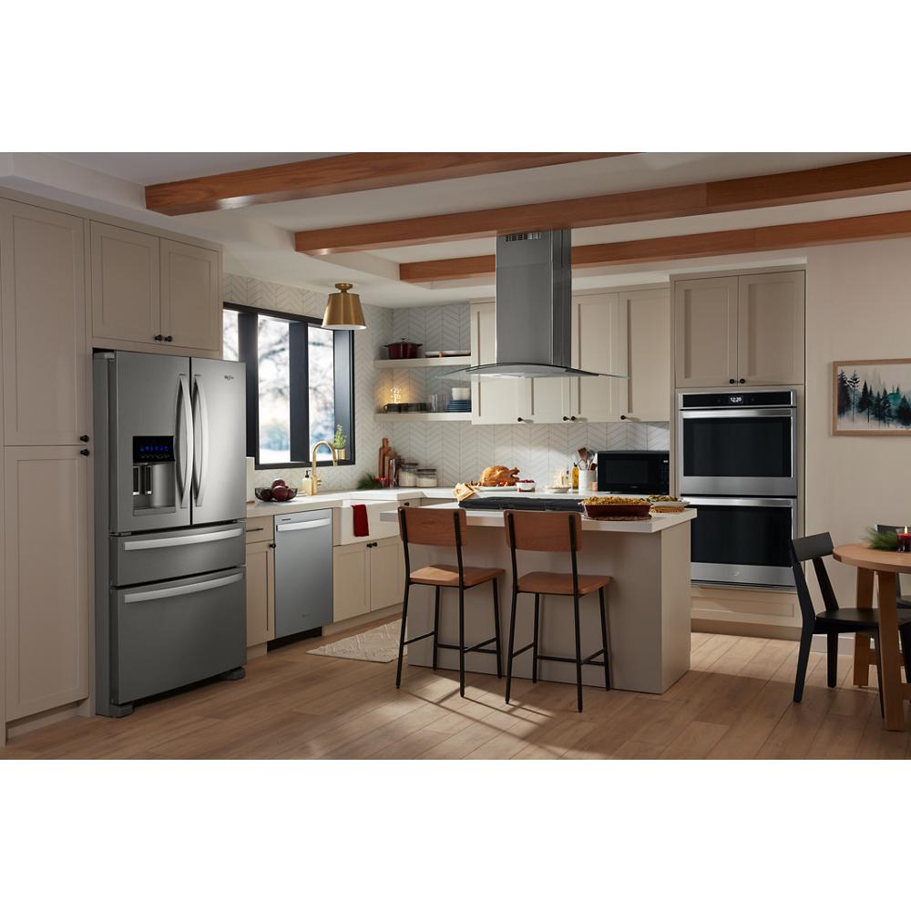 Modern kitchen with beige cabinets, stainless steel refrigerator, double wall oven, dishwasher, and curved glass island range hood