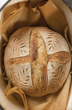 Round artisan bread loaf with decorative leaf scoring pattern on parchment paper in kitchenware and bakeware collections under $50