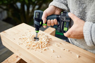 Person using a compact Festool cordless drill to bore holes in a wooden plank for woodworking and power tool tasks