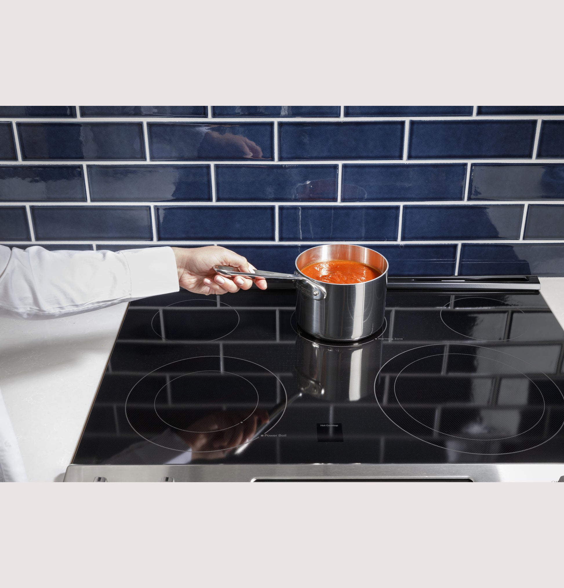 Person stirring tomato sauce in stainless steel saucepan on black glass electric induction cooktop range