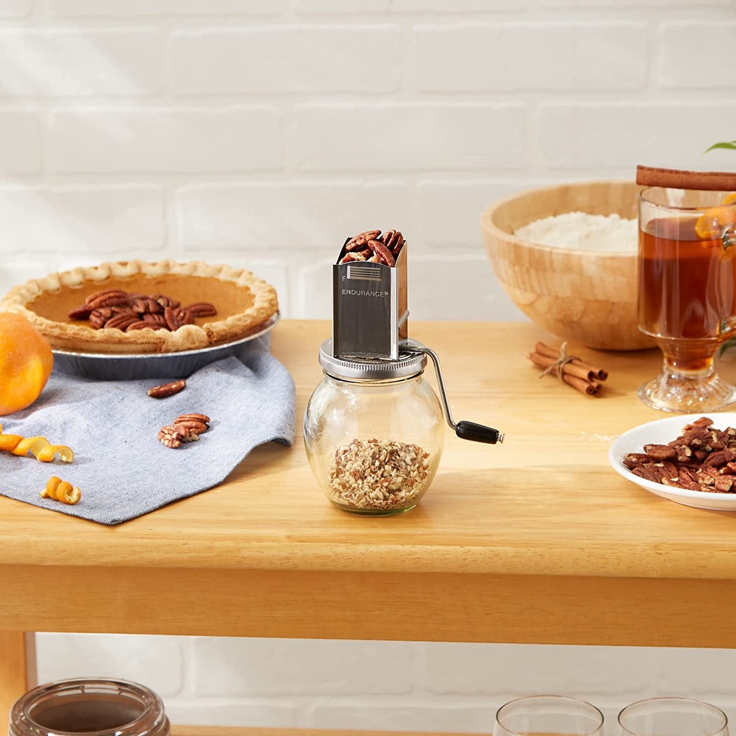 Glass and metal nut grinder with hand crank filled with pecans on wooden kitchen table setting