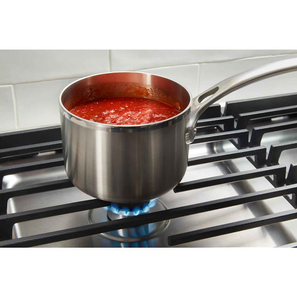 Stainless steel saucepan with tomato sauce heating on blue flame over cast-iron grates of gas cooktop
