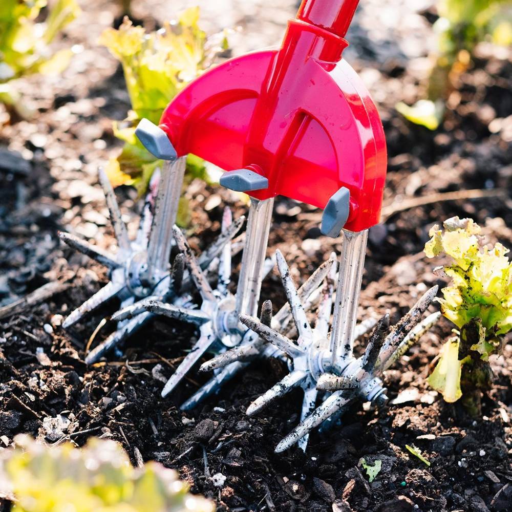 Steel cultivator with red frame and rotating spiked tines digging into garden soil for outdoor gardening tools collections