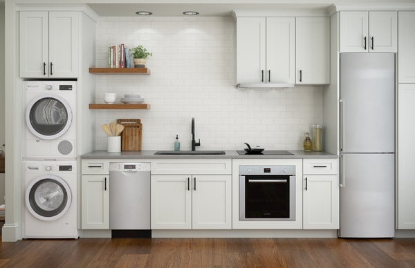 Bright modern kitchen with stainless steel built-in oven, dishwasher, stacked washer-dryer, and refrigerator in white cabinetry