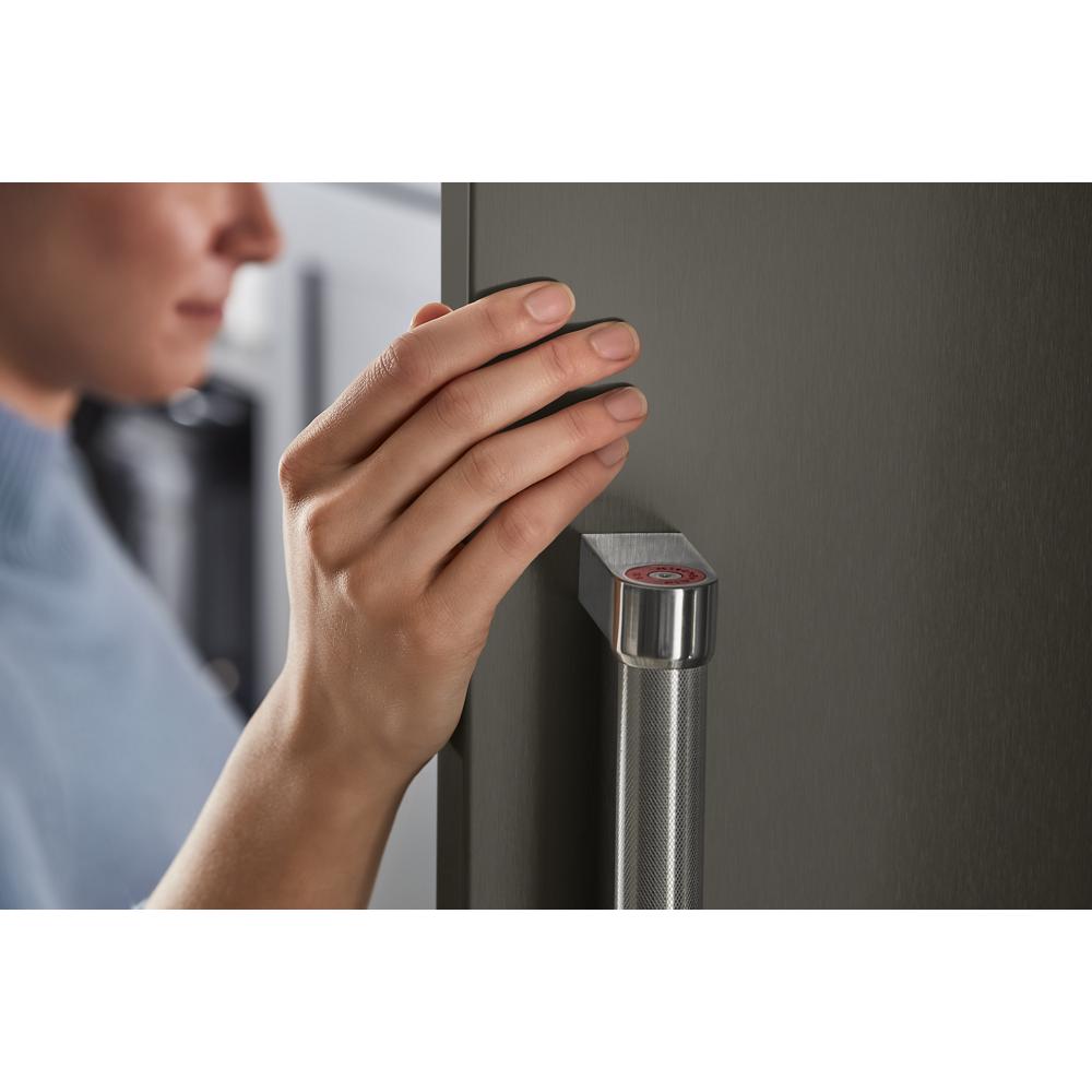 Hand gripping textured stainless steel door handle with red accent on built-in side-by-side refrigerator from KitchenAid Appliances collection